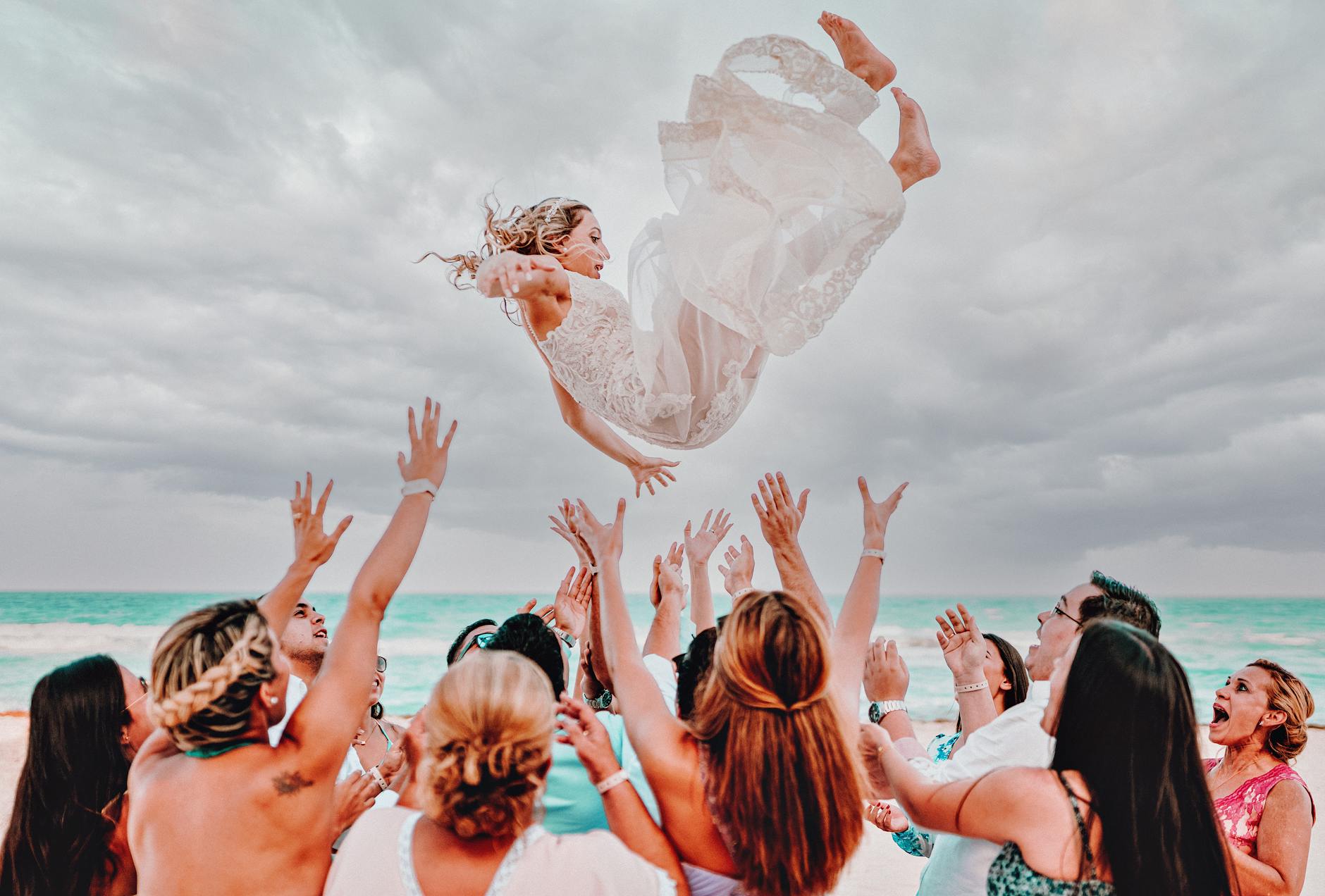 Joyful bride tossed in air during beach wedding in Cancún, Mexico.