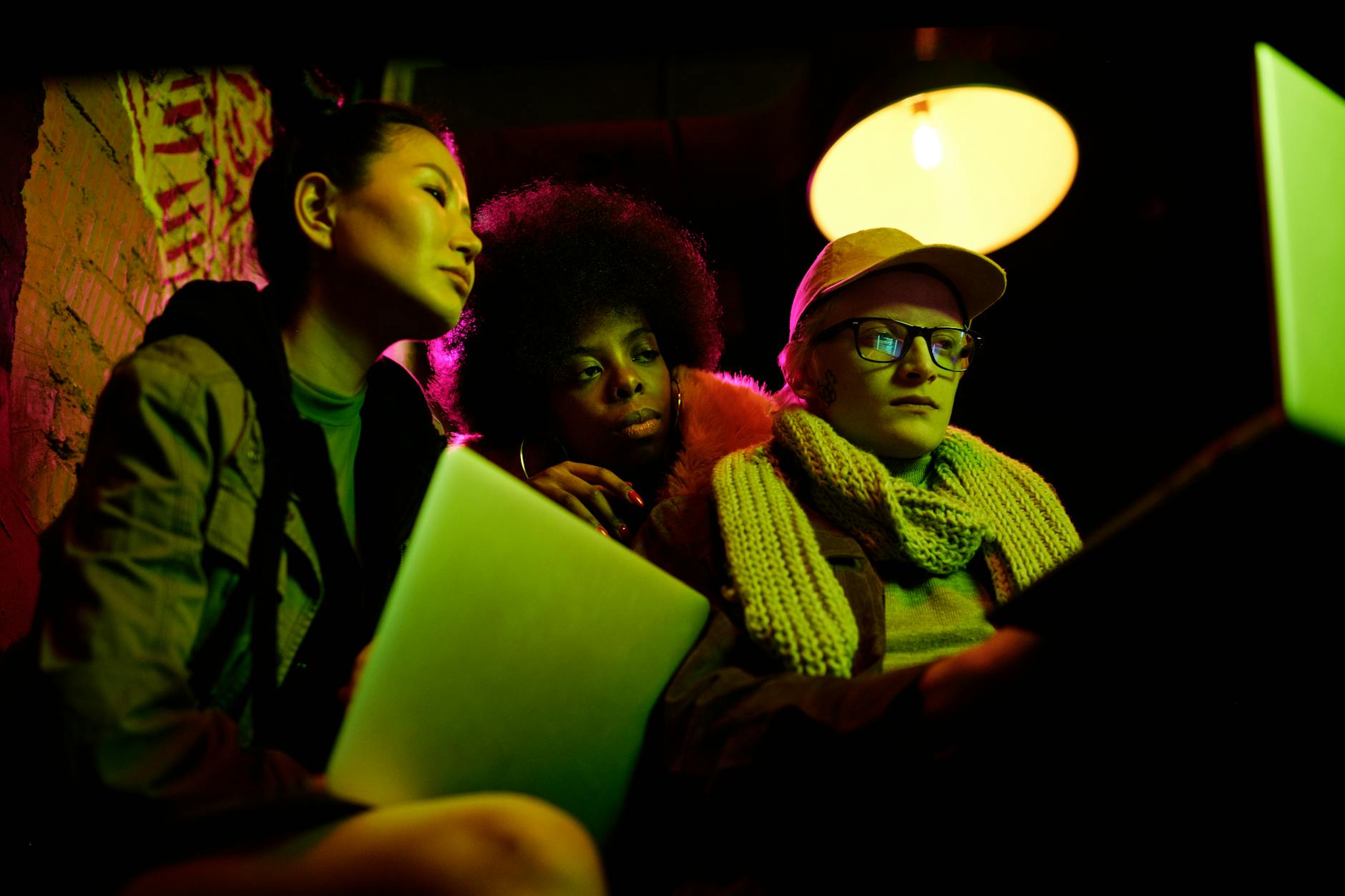 A diverse trio deeply focused on laptops under vibrant lighting, indicating cyber security themes.