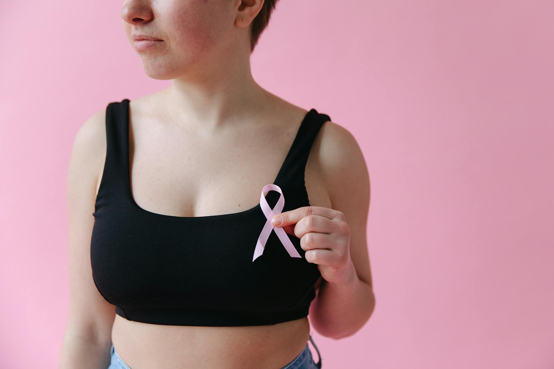 Close-up of a woman holding a pink ribbon symbolizing breast cancer awareness.