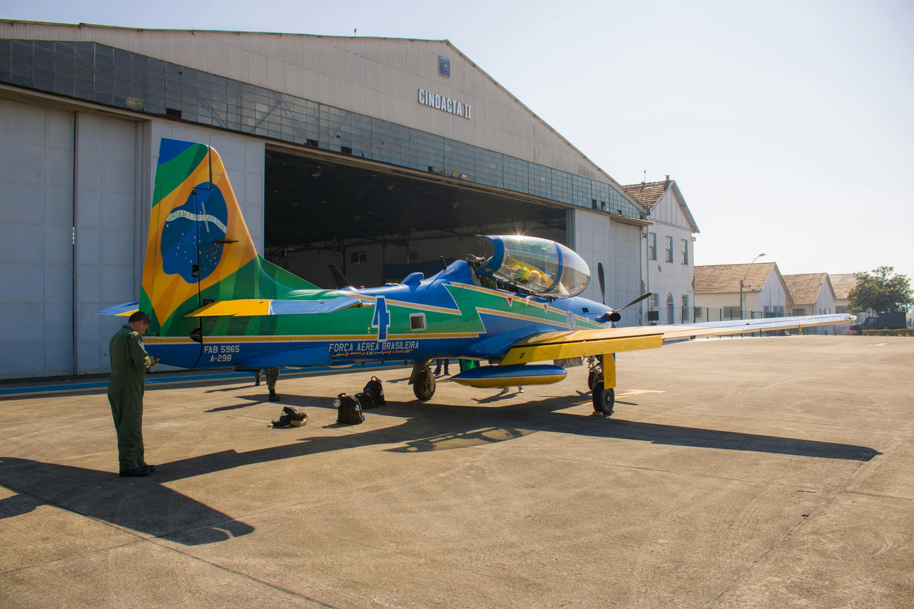 Brazilian Air Force aircraft parked outside a hangar with a military personnel on the tarmac.