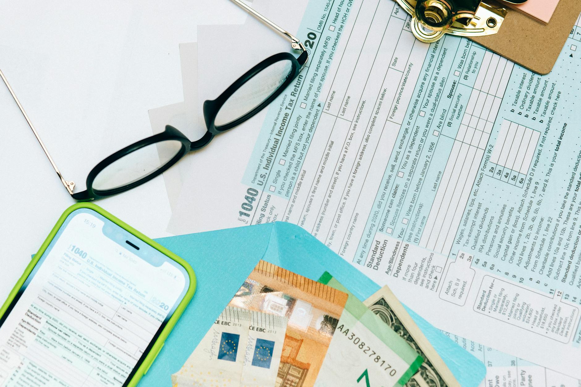 Close-up of tax forms, smartphone, and dollar bills for financial analysis and preparation.